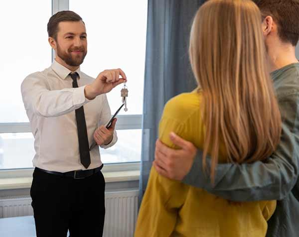 An estate agent handing over a set of property keys to a couple in a Spanish apartment