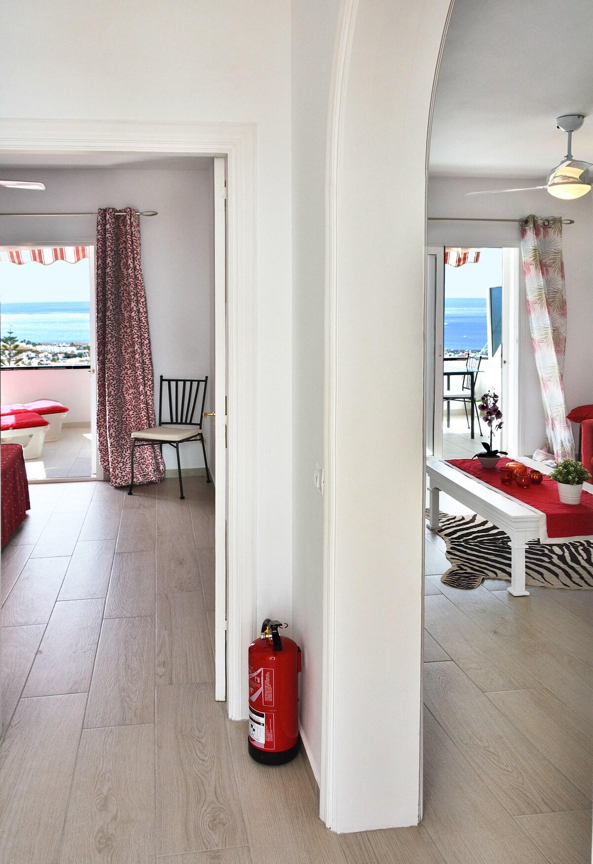 Interior of a prepared Spanish coastal holiday apartment with a fire extinguisher beside the hallway and sea views from the terrace